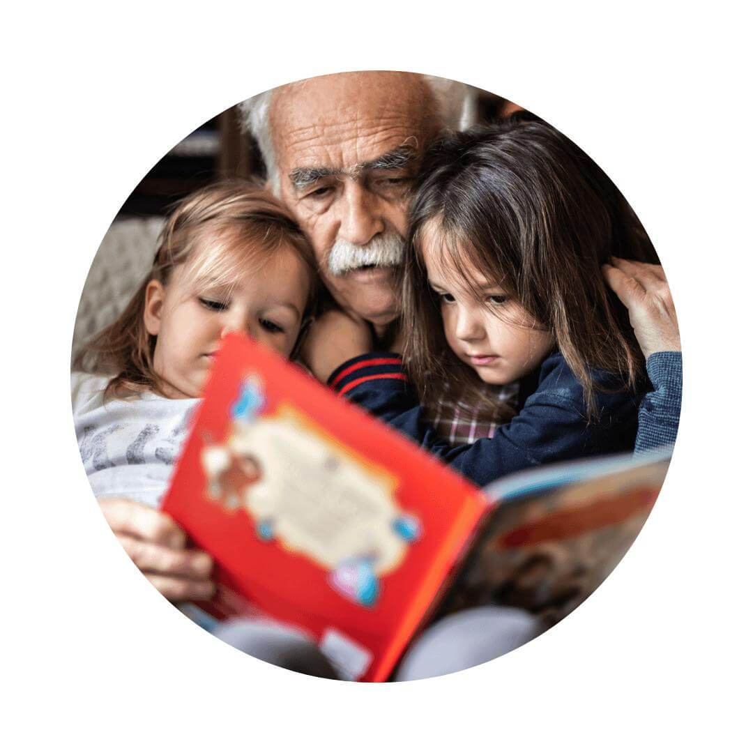 Older man reading a red book to two young children