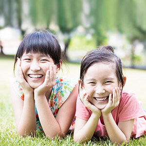 Two young girls smiling and resting on arms outside on grass