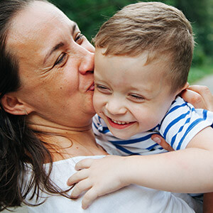 Young boy with blue and white t-shirt smiling and hugging older woman