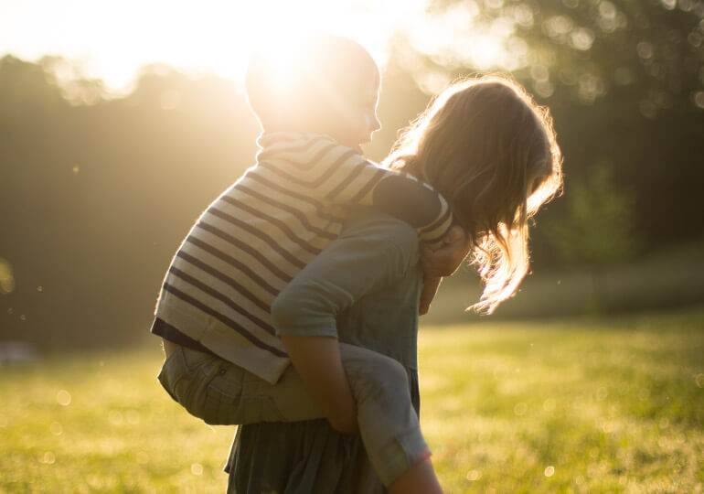 Child on the back of woman walking in a field with the sun shining