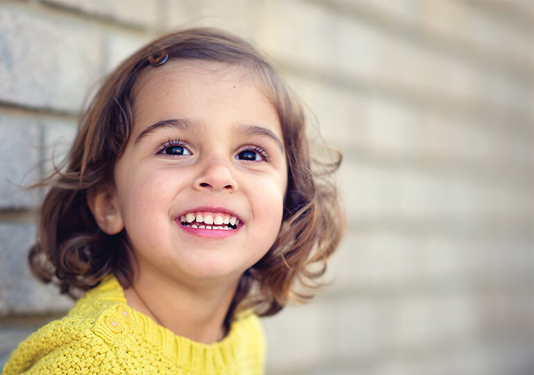 Young girl with brown hair smiling in front of a brick wall