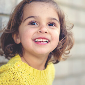 Young girl with brown hair smiling in front of a brick wall