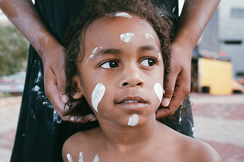 Young aboriginal boy looking away with a person standing behind him