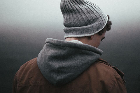 Teenage boy with curly hair in grey beanie standing facing backwards