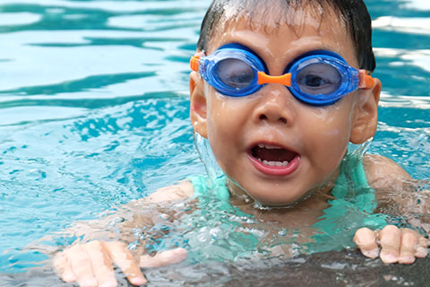 Young boy with goggles on swimming in a pool