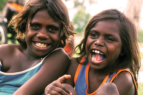 Two aboriginal girls with singlets on smiling outside