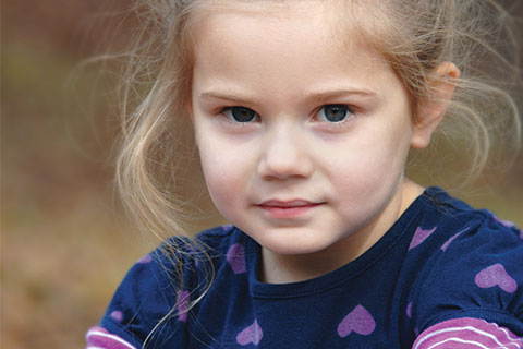 Young girl with blond hair and a blue top with purple hearts outside