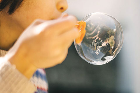 Young child blowing a big bubble outside with people in bubble reflection