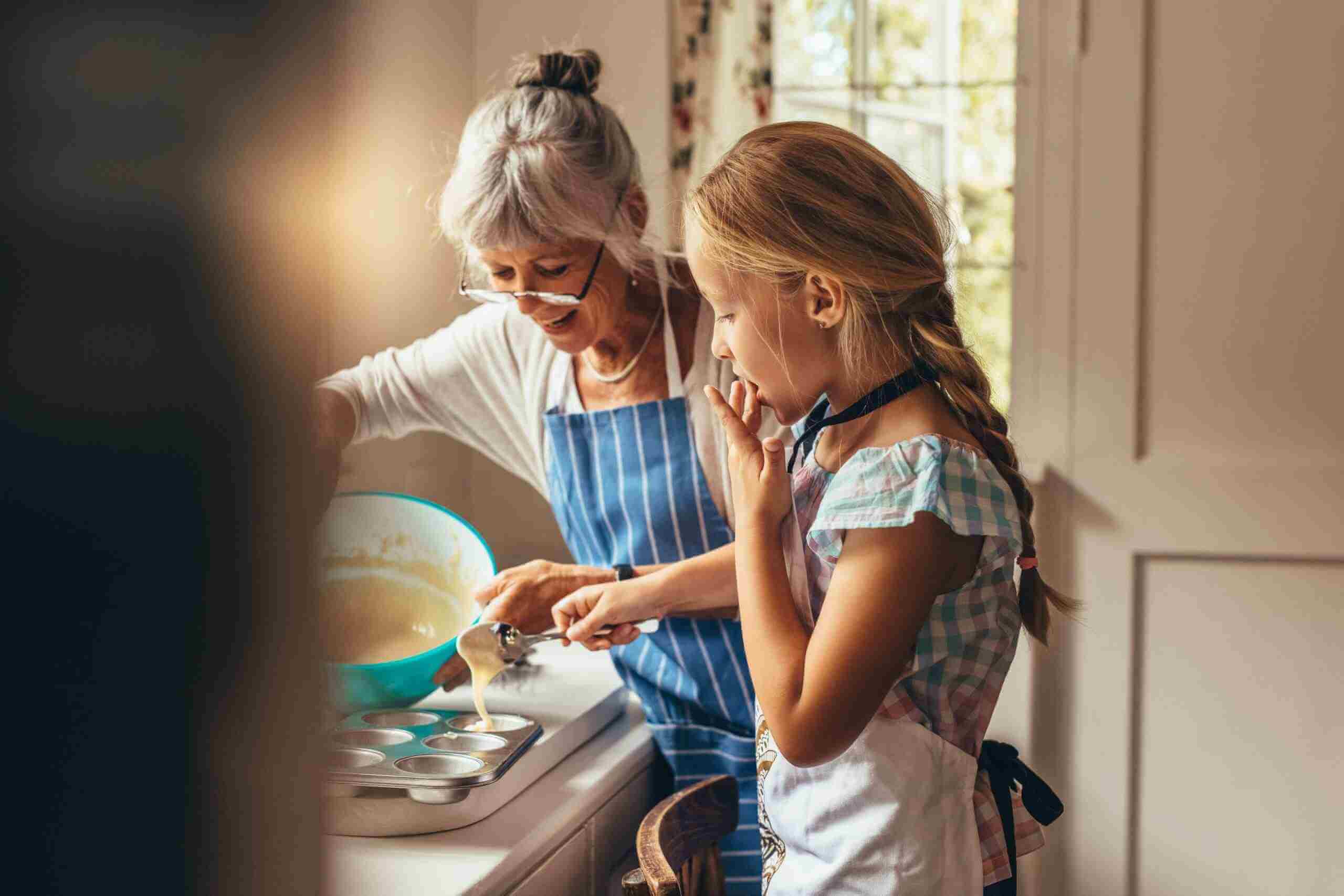 Older woman with grey hair and glasses baking with young girl in the kitchen