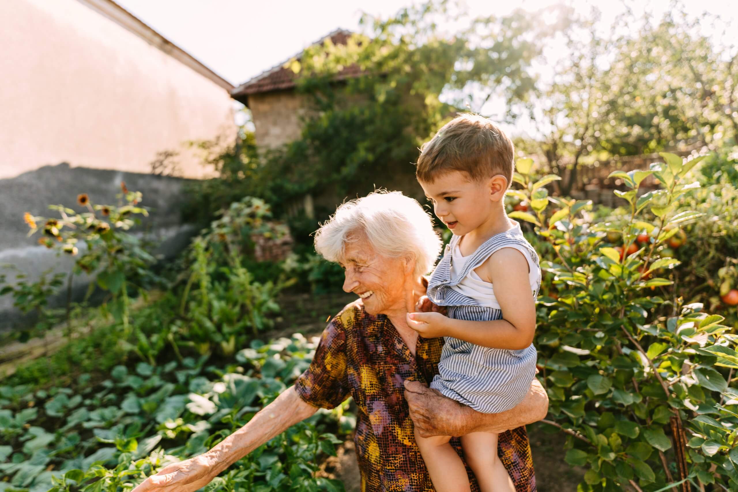 Elderly woman holding a young boy in overalls showing him the garden