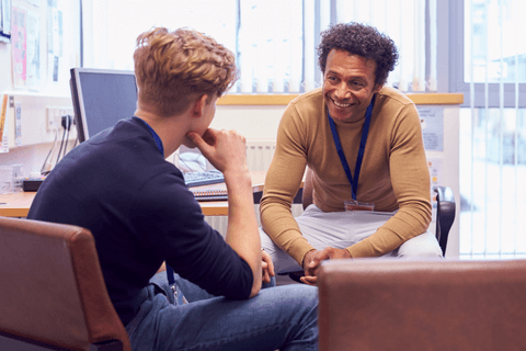 Male therapist talking to adolescent boy with back facing in an office